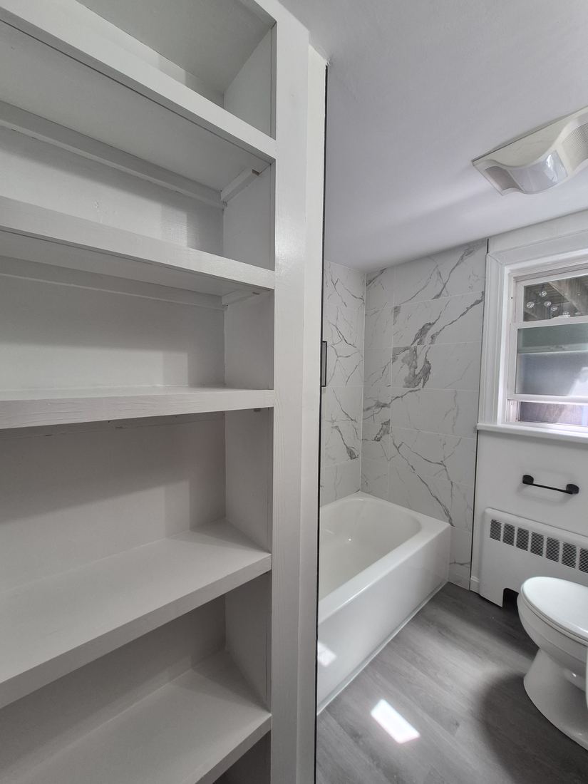 Bathroom in Beverly, MA after remodel with marble-look shower walls, built-in shelving and new flooring