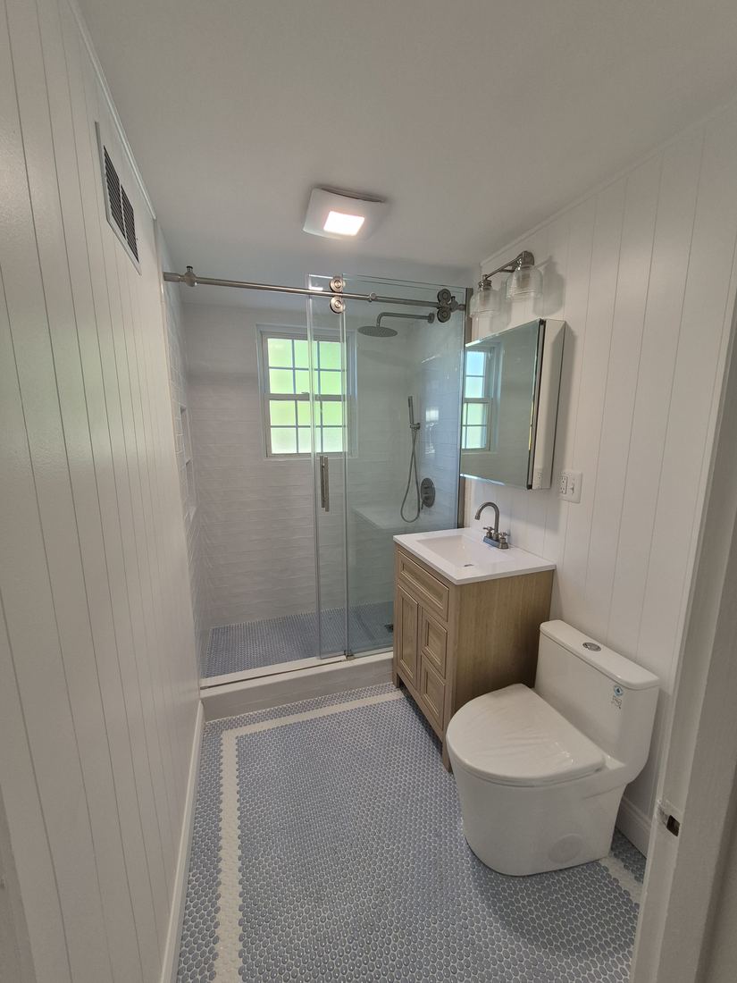 Bathroom in Danvers, MA after remodel with glass shower, white paneling, wood vanity and blue hex floor tile