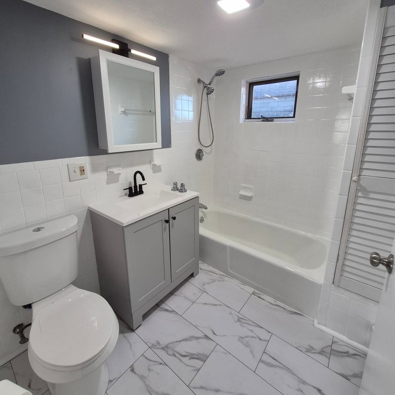 Bathroom after refresh in Lynn, MA with new gray vanity, black fixtures, white tile and marble-look floor