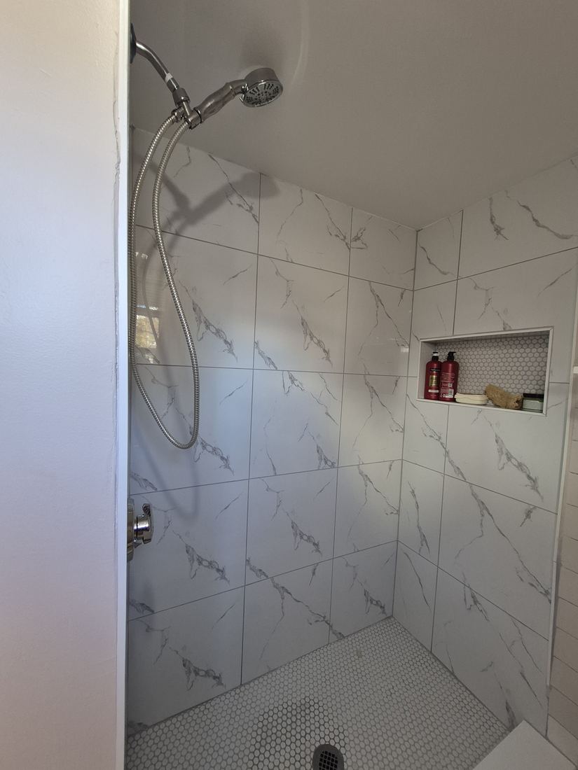 Tiled shower in Lynn, MA after tub-to-shower conversion with marble-look tile and built-in niche