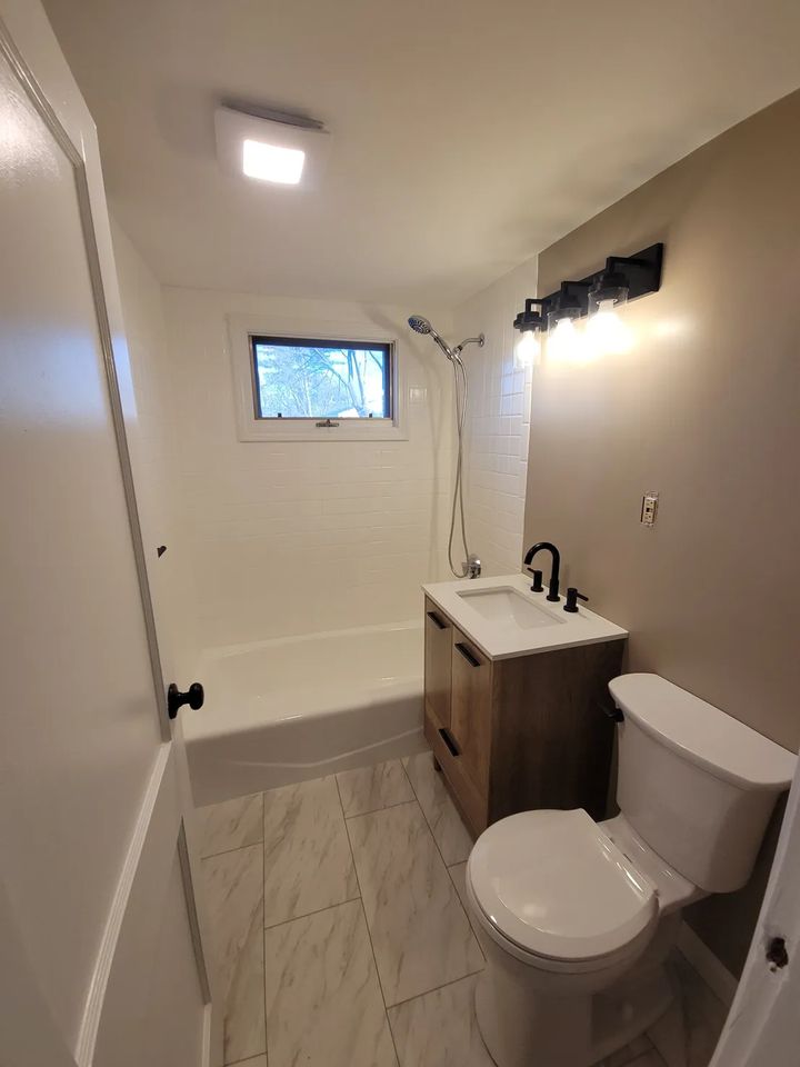 Bathroom after refresh in Peabody, MA with new wood-look vanity, black fixtures, white shower walls and marble-look floor
