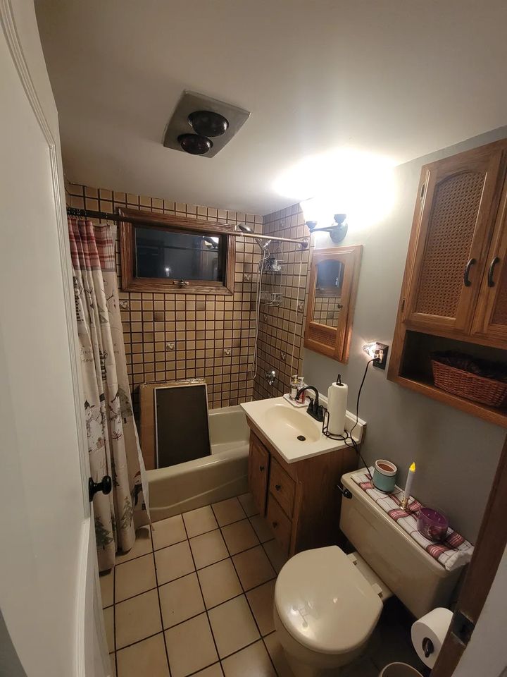 Bathroom before refresh in Peabody, MA with brown grid tile, oak vanity and beige fixtures