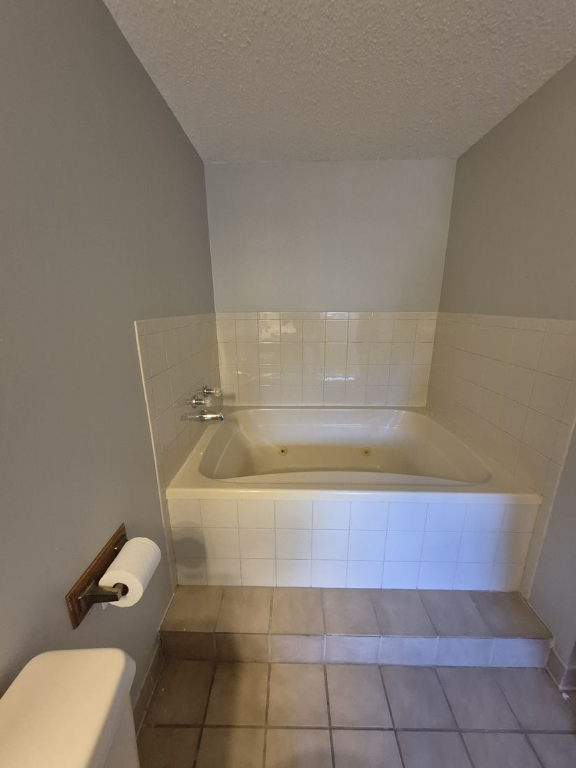 Jetted tub in Salem, MA before remodel with white tile deck and brown floor tile